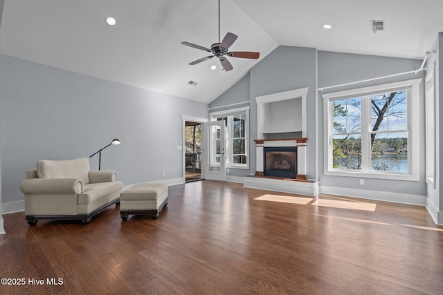 living area with ceiling fan, plenty of natural light, a fireplace with raised hearth, and wood finished floors