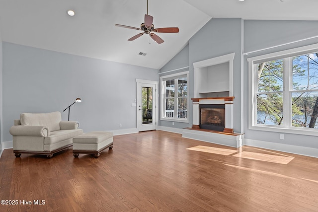 unfurnished room featuring plenty of natural light, a fireplace with raised hearth, ceiling fan, and wood finished floors