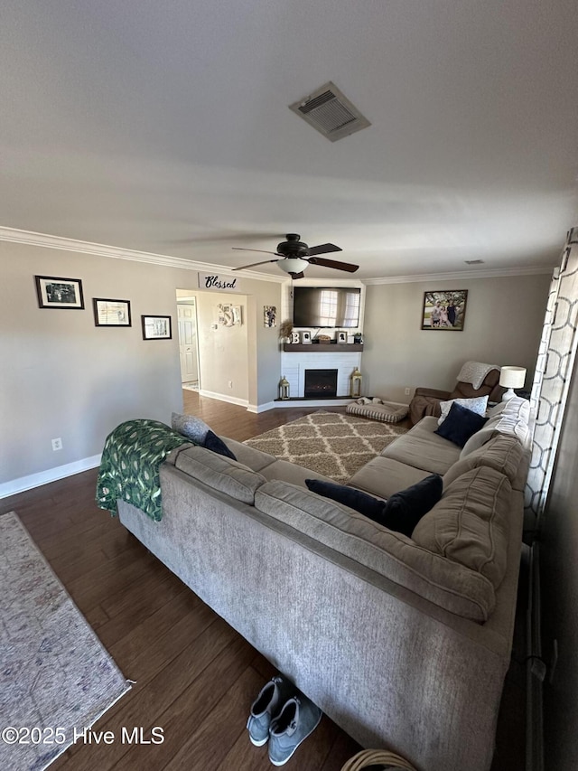 living room with a fireplace with raised hearth, wood finished floors, visible vents, baseboards, and ornamental molding