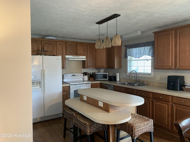 kitchen with appliances with stainless steel finishes, dark wood-type flooring, light countertops, under cabinet range hood, and a sink