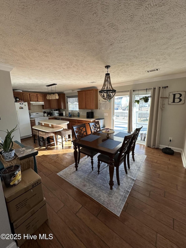 dining area featuring baseboards, dark wood finished floors, visible vents, and crown molding