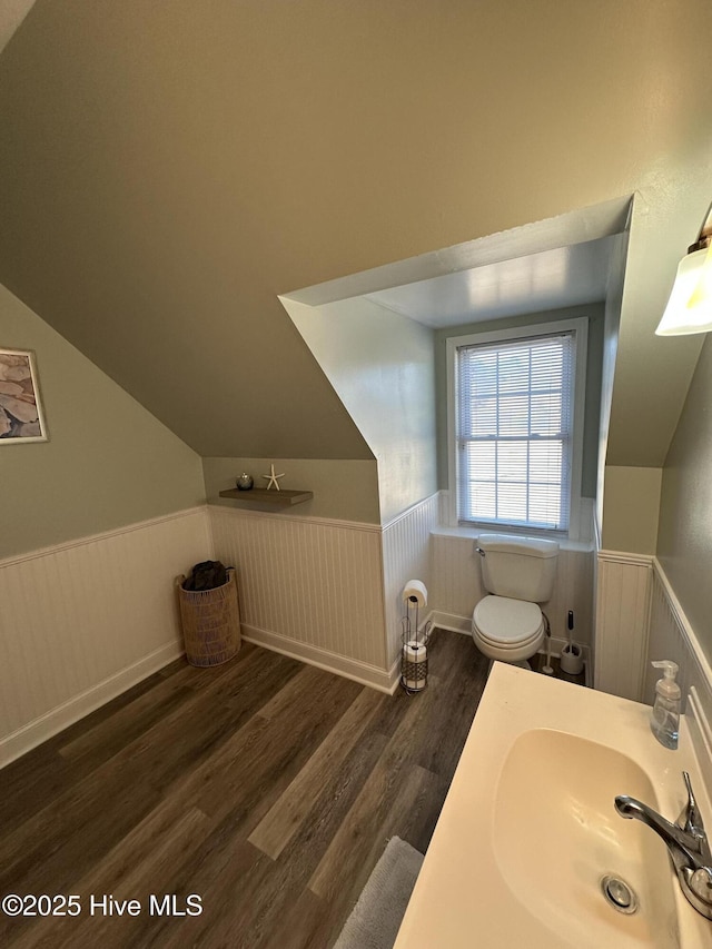 bathroom with toilet, a wainscoted wall, lofted ceiling, wood finished floors, and a sink