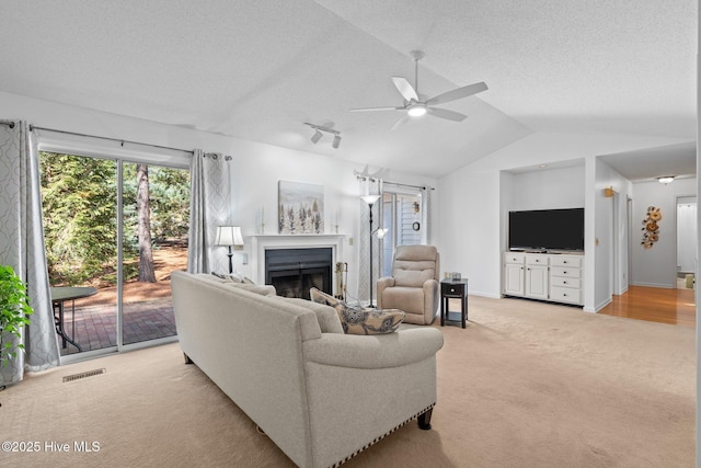 living area featuring visible vents, lofted ceiling, light carpet, a fireplace, and a textured ceiling