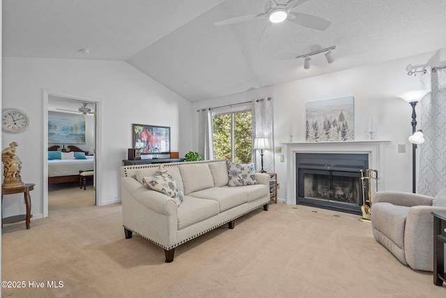 living room featuring a ceiling fan, a fireplace with flush hearth, vaulted ceiling, a textured ceiling, and light carpet