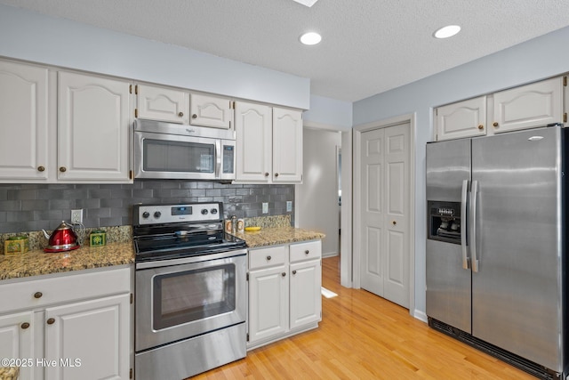 kitchen with light wood finished floors, white cabinets, appliances with stainless steel finishes, and tasteful backsplash