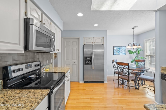 kitchen with tasteful backsplash, light stone counters, appliances with stainless steel finishes, and light wood-style floors