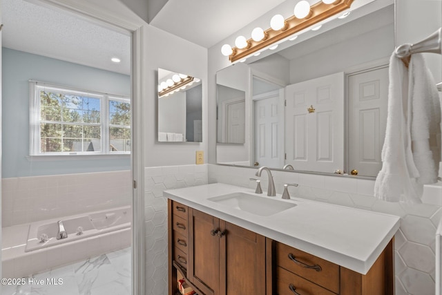 full bathroom with a garden tub, a textured ceiling, tile walls, wainscoting, and vanity