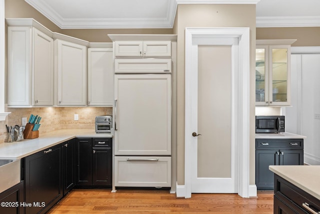 kitchen with stainless steel microwave, white cabinets, light wood-style floors, and paneled built in fridge