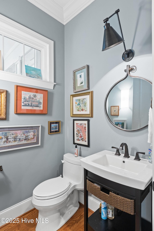 half bath featuring toilet, ornamental molding, a sink, wood finished floors, and baseboards