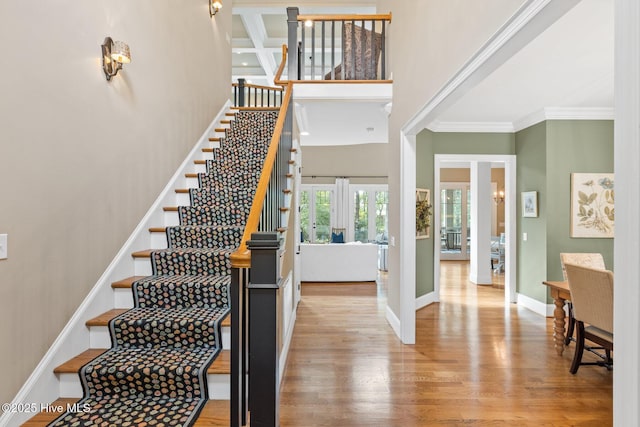 stairs featuring crown molding, baseboards, beamed ceiling, a high ceiling, and wood finished floors