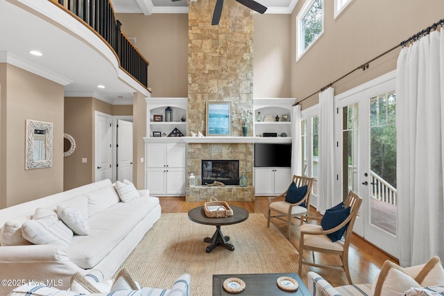 living area with a high ceiling, a fireplace, ornamental molding, french doors, and light wood-type flooring