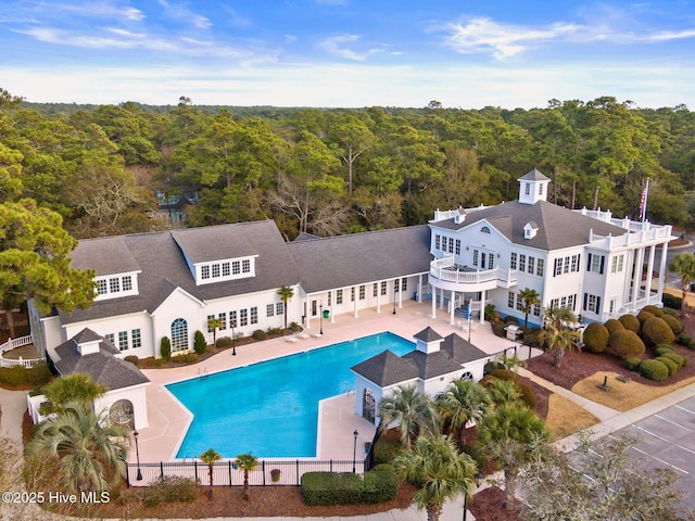 exterior space with a fenced in pool, fence, a view of trees, a balcony, and a patio area