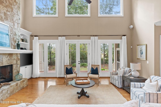 living room with french doors, light wood-style floors, a high ceiling, and a fireplace