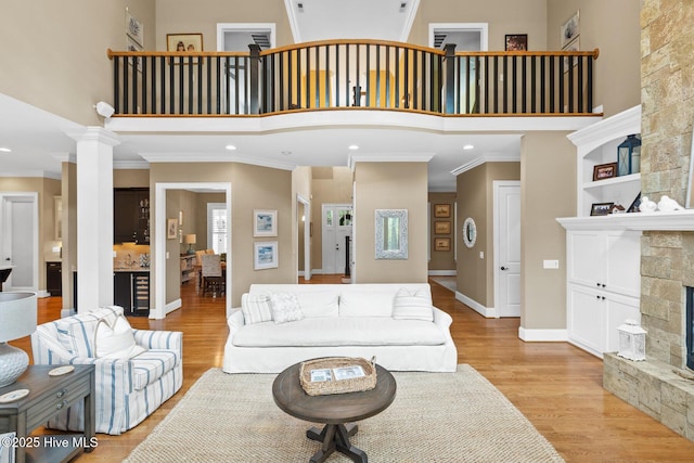 living room with a high ceiling, light wood-style flooring, a fireplace, and crown molding