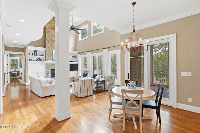 dining room with crown molding, baseboards, decorative columns, a stone fireplace, and light wood-style floors