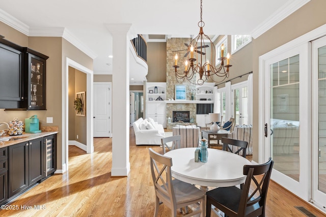 dining area featuring beverage cooler, visible vents, light wood-style flooring, a fireplace, and crown molding