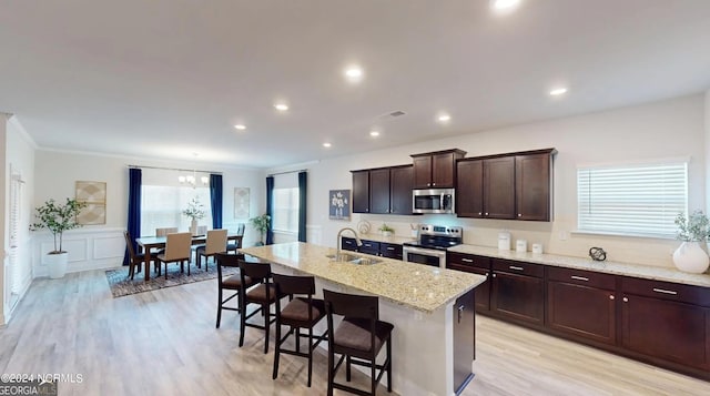 kitchen with light wood-style flooring, a breakfast bar, a sink, dark brown cabinets, and appliances with stainless steel finishes