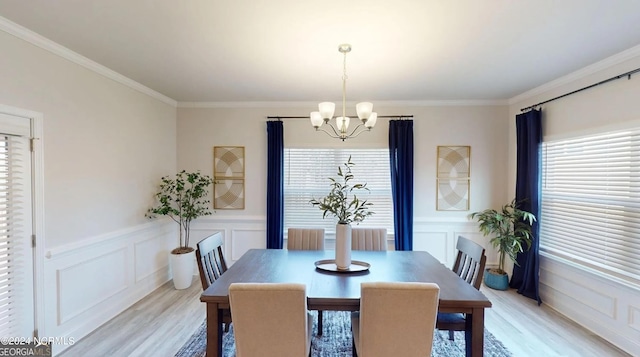 dining room featuring a decorative wall, a wainscoted wall, ornamental molding, light wood-type flooring, and an inviting chandelier