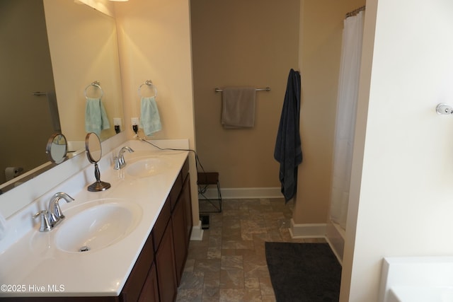 bathroom featuring double vanity, stone finish flooring, baseboards, and a sink