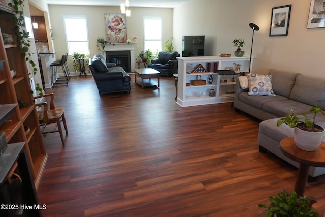 living room with a glass covered fireplace, dark wood-type flooring, and baseboards