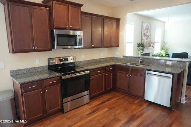 kitchen with dark stone counters, appliances with stainless steel finishes, a peninsula, dark wood-style floors, and a sink