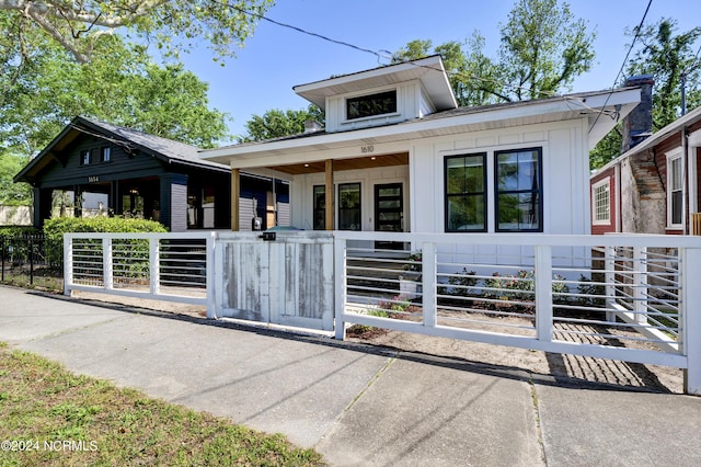 bungalow-style home with covered porch, board and batten siding, and fence