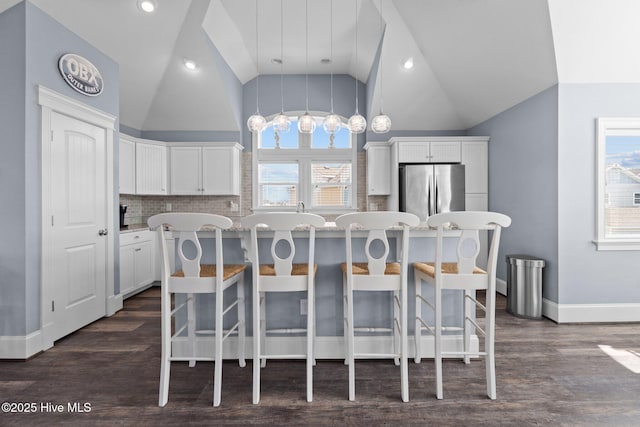 kitchen featuring a kitchen breakfast bar, a kitchen island, white cabinetry, freestanding refrigerator, and lofted ceiling