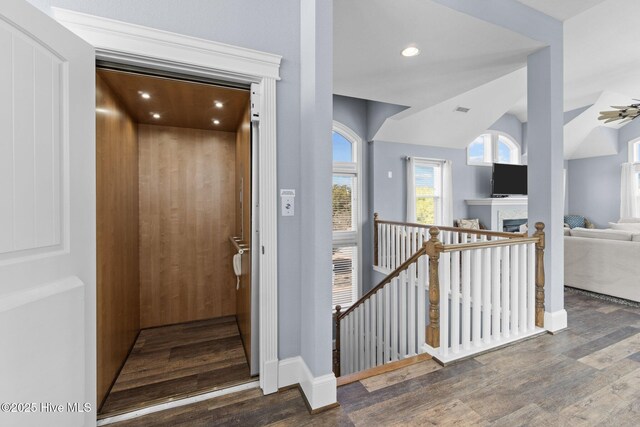 stairway featuring visible vents, lofted ceiling, elevator, a fireplace, and wood finished floors