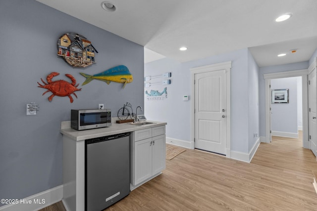 kitchen with baseboards, a sink, light countertops, stainless steel microwave, and light wood-type flooring