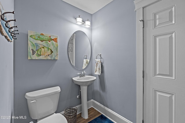 half bath with a sink, baseboards, toilet, and wood finished floors