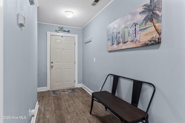 entryway featuring a textured ceiling, wood finished floors, visible vents, baseboards, and ornamental molding