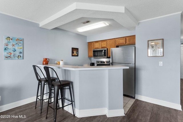 kitchen featuring brown cabinetry, dark wood-style floors, a breakfast bar area, a peninsula, and stainless steel appliances