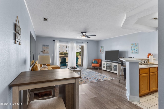 living room featuring a ceiling fan, visible vents, a textured ceiling, and light wood finished floors