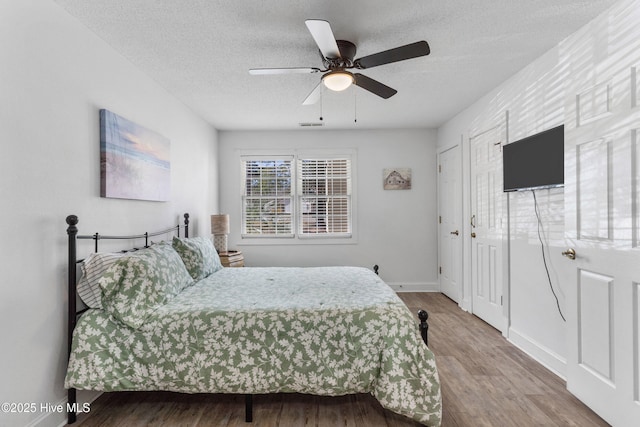 bedroom with a textured ceiling, wood finished floors, visible vents, a ceiling fan, and baseboards