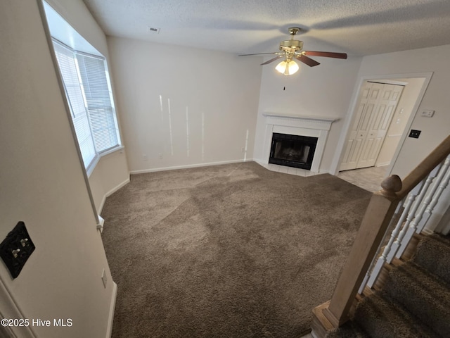 unfurnished living room with a fireplace with flush hearth, carpet, a textured ceiling, and stairs