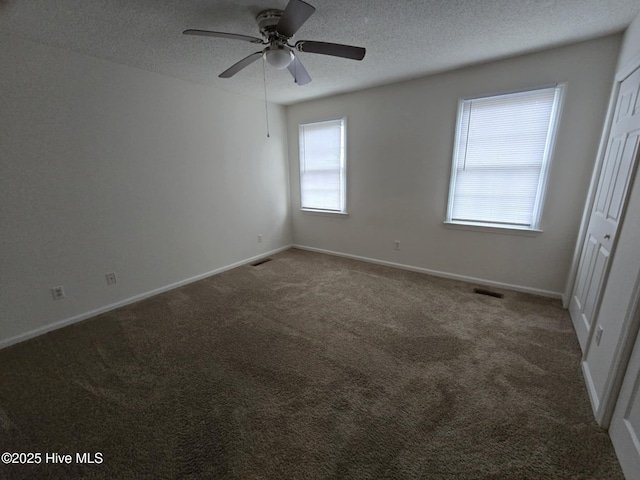 spare room featuring carpet floors, visible vents, a textured ceiling, and baseboards