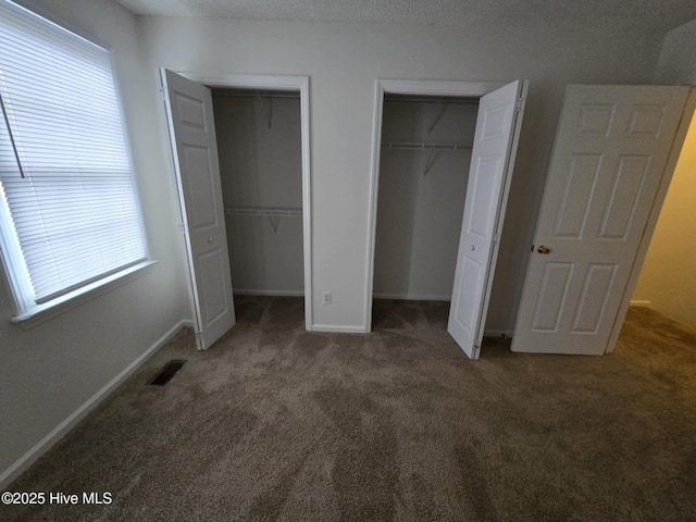 unfurnished bedroom with carpet, visible vents, baseboards, and two closets