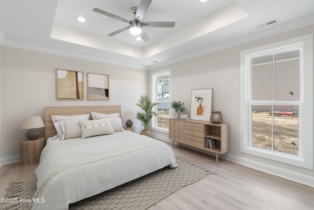 bedroom with visible vents, light wood-style flooring, a tray ceiling, crown molding, and baseboards