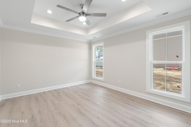 spare room featuring visible vents, a tray ceiling, light wood finished floors, baseboards, and ceiling fan