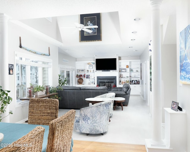 living area with a glass covered fireplace, decorative columns, wood finished floors, and ceiling fan