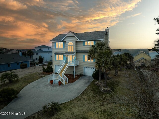 beach home featuring concrete driveway, stairway, an attached garage, and a chimney