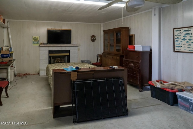 living room with unfinished concrete flooring, a tiled fireplace, wood walls, ornamental molding, and a ceiling fan