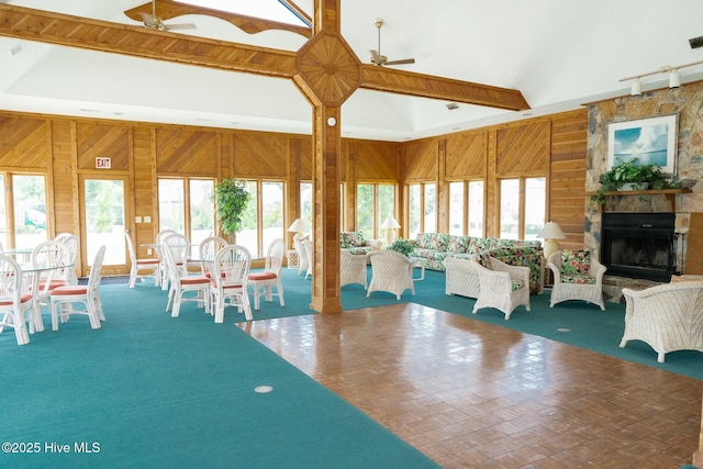 unfurnished dining area with wooden walls, a ceiling fan, high vaulted ceiling, a fireplace, and rail lighting