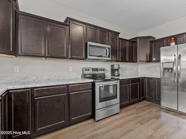 kitchen with light wood-style flooring, a textured ceiling, stainless steel appliances, light countertops, and dark brown cabinets