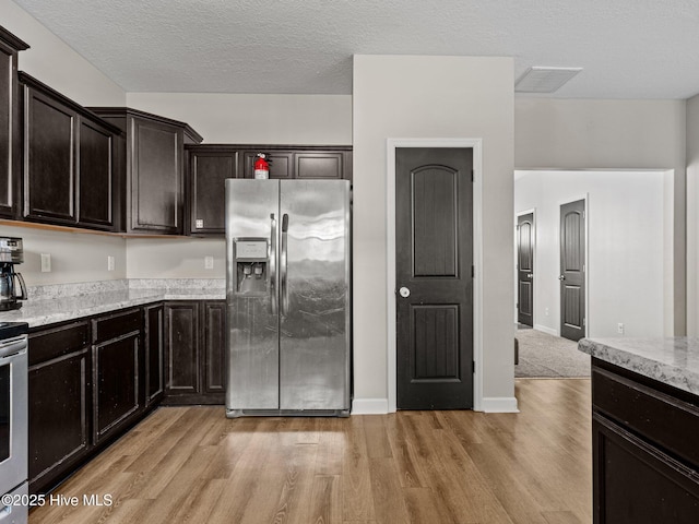 kitchen featuring light wood-type flooring, visible vents, a textured ceiling, stainless steel fridge with ice dispenser, and light stone countertops