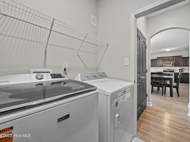 clothes washing area with visible vents, washing machine and clothes dryer, laundry area, arched walkways, and light wood-type flooring