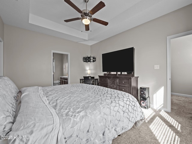 bedroom featuring a tray ceiling, carpet, ensuite bath, and ceiling fan