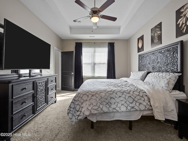 bedroom featuring a tray ceiling, light carpet, and ceiling fan