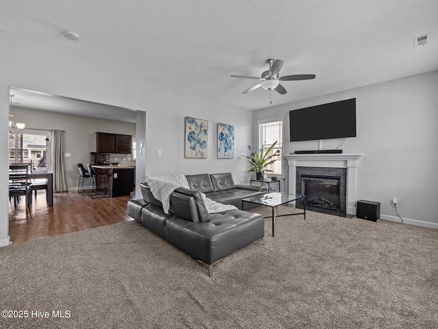 living area featuring visible vents, a textured ceiling, a fireplace with flush hearth, and carpet floors