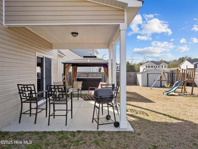 view of patio with a fenced backyard, a hot tub, a gazebo, a storage unit, and a playground